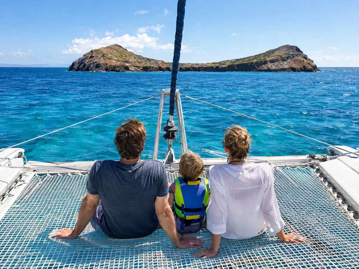 Eine Familie sitzt auf dem Bugnetz eines Katamarans, ein Kind in Schwimmweste, vor ihnen Molokini